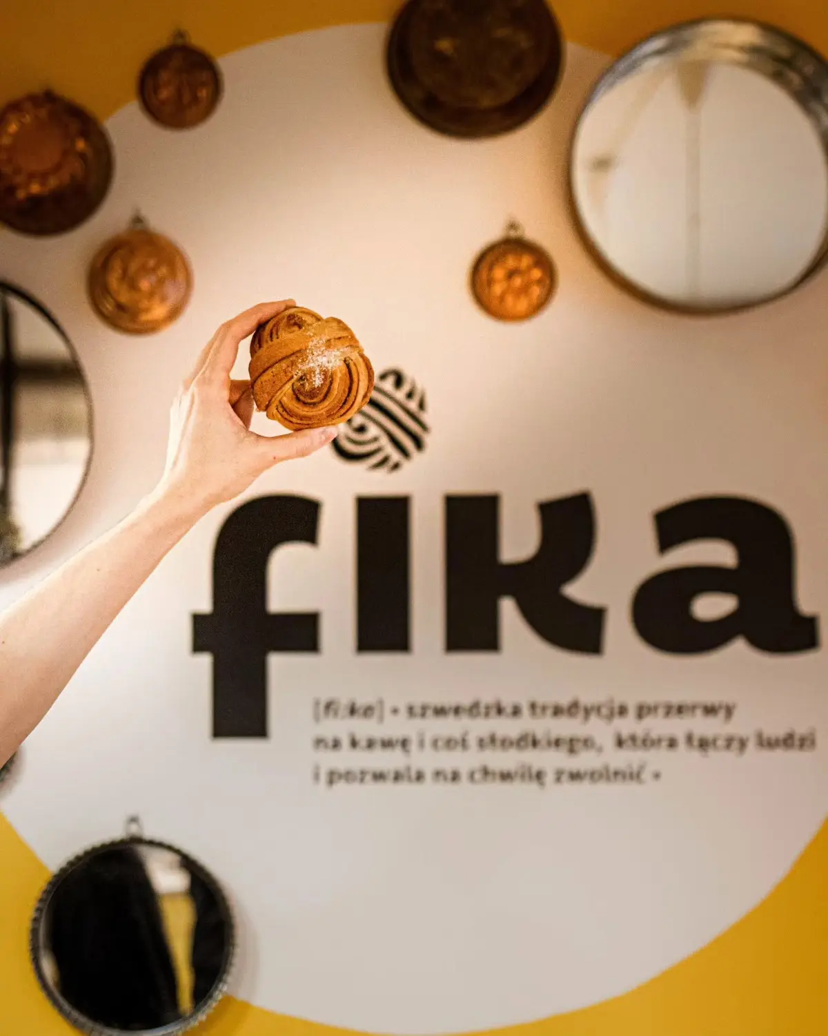 Świeżo wypieczona kardamonka trzymana na tle logo FIKA